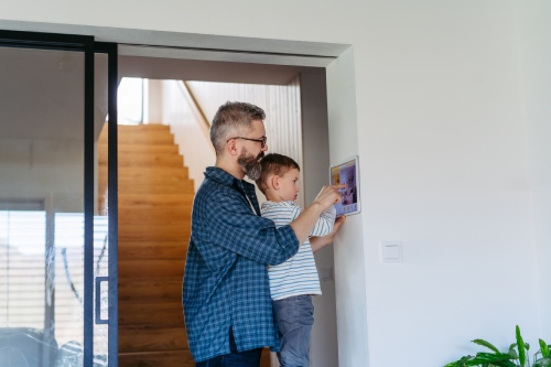 Father showing son smart home system, adjusting household functions, lighting, security cameras, door locks and smart thermostat or heating settings. Concept of sustainable and smart technology in