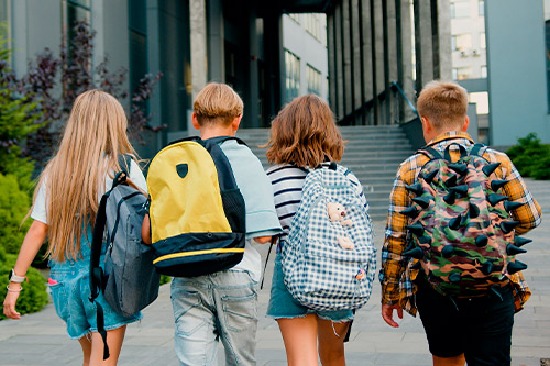 A group of four young individuals carrying backpacks strolls down a street, highlighting a welcoming environment for families.