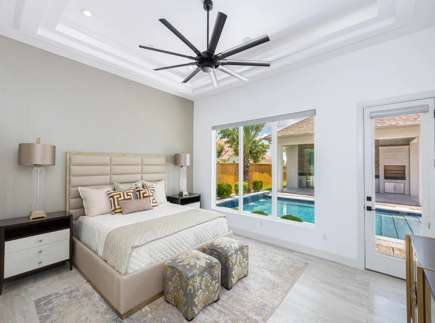 Modern bedroom featuring a large bed, decorative stools, and a view of a pool through a large window.