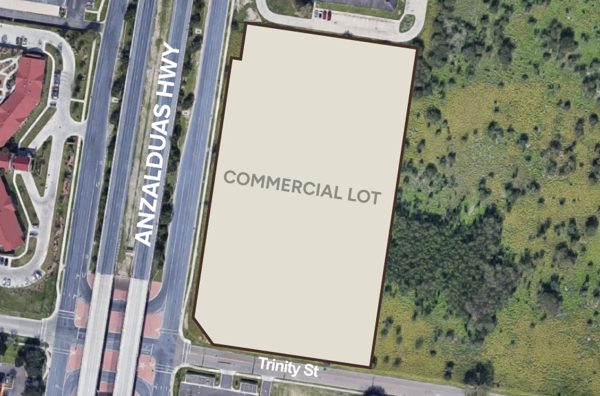 Aerial view of a vacant commercial lot bordered by Anzalduas Highway and Trinity Street, surrounded by greenery.