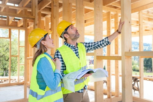 Construction engineer and architect consult plans on building site of wood framing house under construction